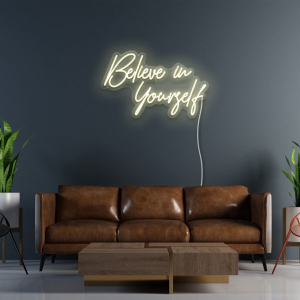 Believe in Yourself CUSTOM NEON® pre-designed light sign shown in warm white on dark wall above a brown couch