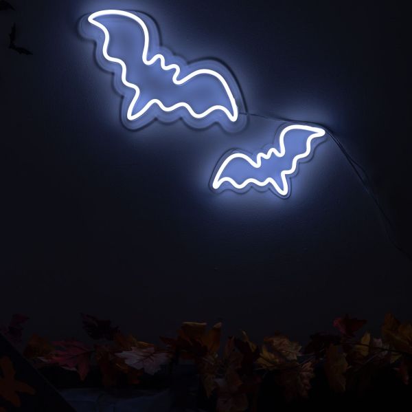 Custom Neon® Halloween bat signs shown in white LED neon wall mounted over autumn leaves.