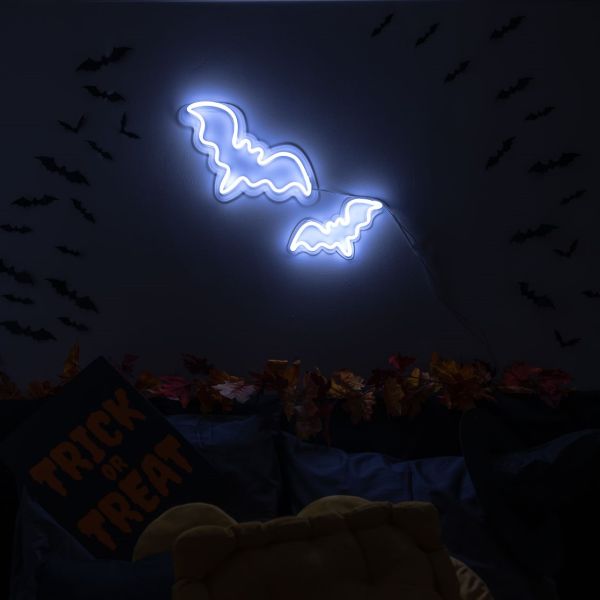 Custom Neon® Halloween bat signs shown in white LED neon wall mounted over autumn leaves.