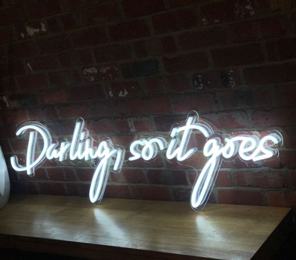 Beautiful cursive neon word sign * Darling, so it goes * shown against exposed brick wall
 - photo from Custom Neon by Neon Collective