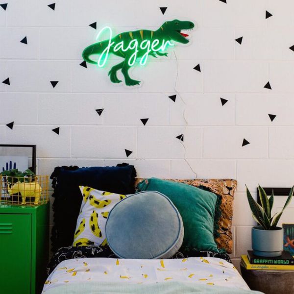 Personalised LED neon child's name sign with dinosaur background shown in child's bedroom- from Custom Neon by Neon Collective