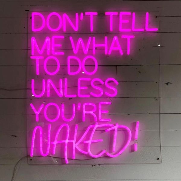 Don't Tell Me What to do Unless You're Naked pink LED sign from Custom Neon® shown on a white paneled wall
