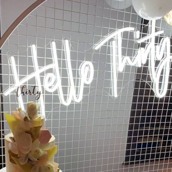 Hello Thirty Light Up Birthday Sign shown in white on mesh in front of the birthday cake - photo from CustomNeon.com.au