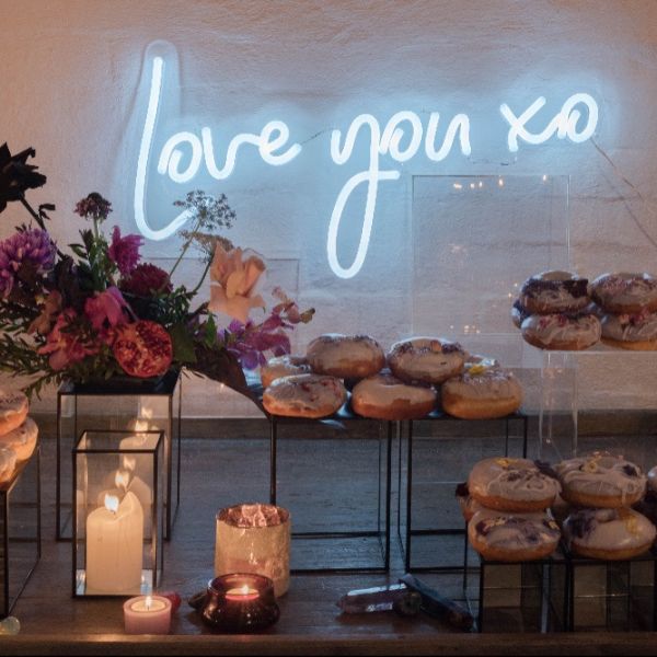 Love You XO LED neon light shown wall mounted behind the sweets table at an event - from CustomNeon.com.au