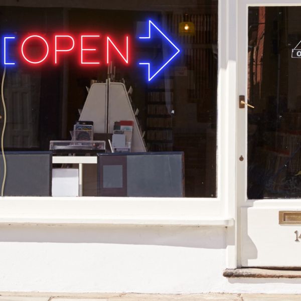 Neon light open sign in red with an oversized blue arrow shown in a shop window - from CustomNeon.com.au