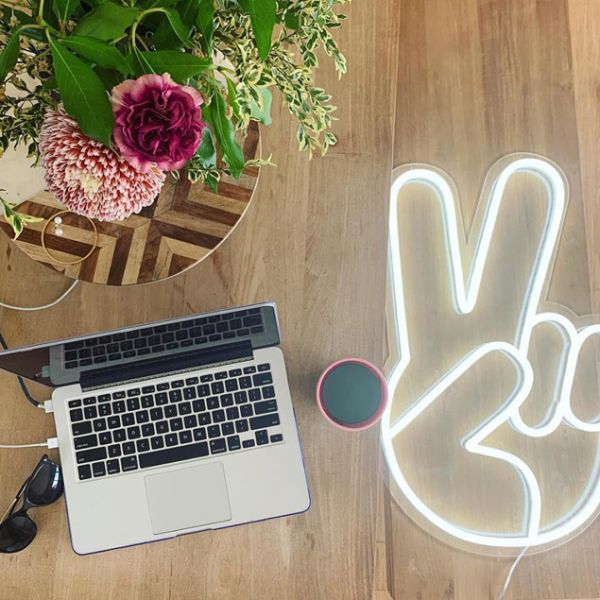LED Neon Peace Sign Light shown on wooden floor - Photo Custom Neon by Neon Collective