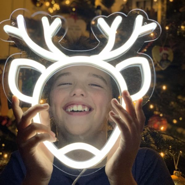 CUSTOM NEON® Reindeer white light sign held by a child with a Christmas tree in the background