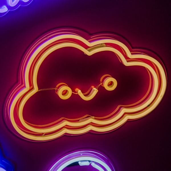 Smiley Cloud LED wall light in warm white shown illuminated against a dark background in dim light - CUSTOM NEON®