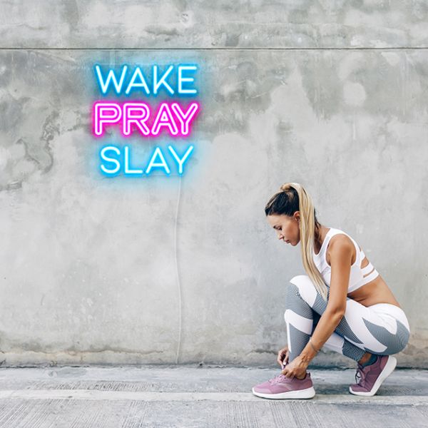 Wake Pray Slay Neon Sign in blue & pink on mottled grey wall on a running track
