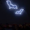 Custom Neon® Halloween bat signs shown in white LED neon wall mounted over autumn leaves.