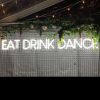 EAT DRINK DANCE large LED neon sign for events & weddings, shown on wire mesh with floral arrangement & fairy lights - photo from CustomNeon.com.au