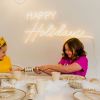 CUSTOM NEON® warm white Happy Holidays light sign wall mounted above a children's Christmas party.