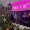 Custom Neon® pink LOVE IS LOVE light sign shown wall mounted above a TV in a living room