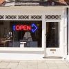 Neon light open sign in red with an oversized blue arrow shown in a shop window - from CustomNeon.com.au