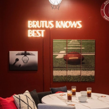 Warm white Custom Neon® sign featuring Manhattan double-lined font on a burnt umber wall