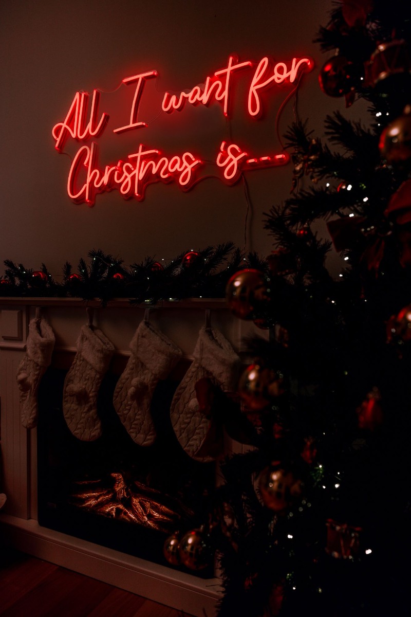 Custom Neon® All I Want for Christmas is... song lyric sign above the mantlepiece surrounded by seasonal decorations