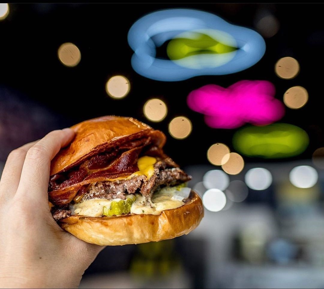 Instagram post @crackedeggery showing a burger in the foreground and Custom Neon® signs on the ceiling