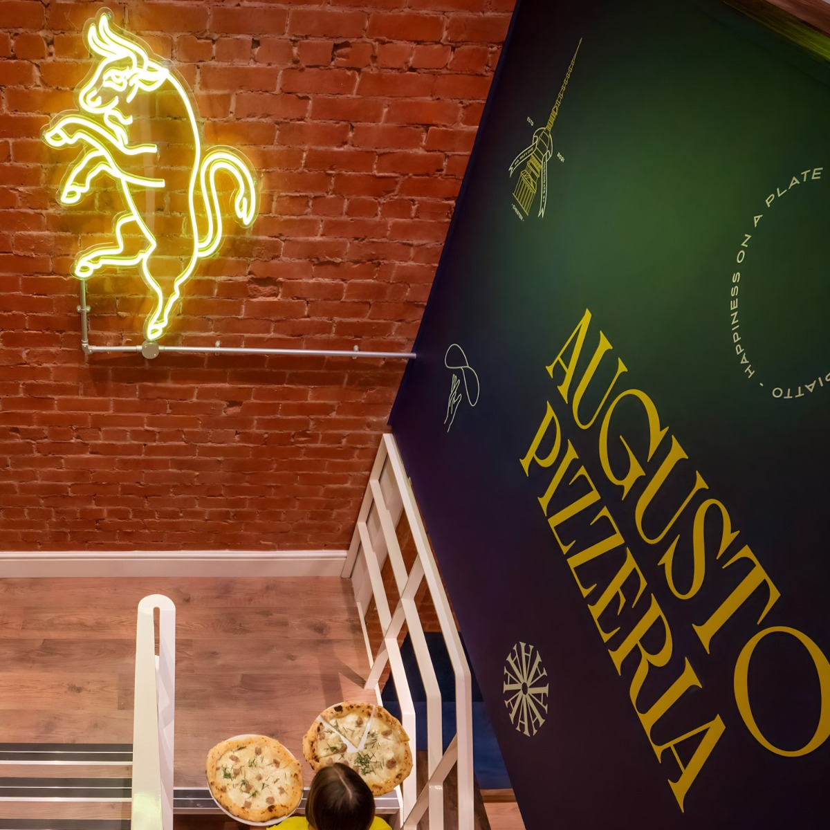 Custom Neon® yellow bull artwork on brick wall on the staircase at @augustopizzeriachester