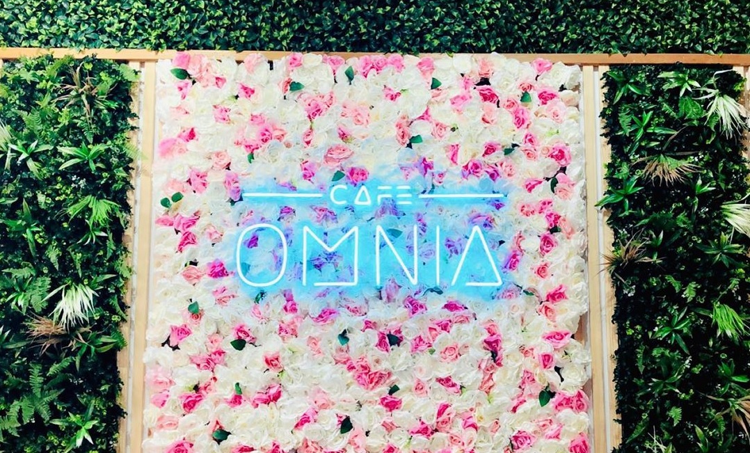 Blue logo sign by Custom Neon® on floral wall @cafeomnia 