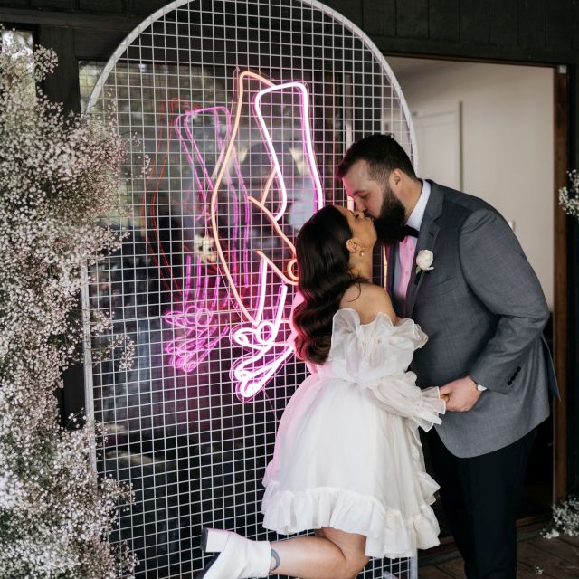 Custom Neon® holding hands artwork sign on a white wire mesh frame behind the bride and groom @hellochloemay