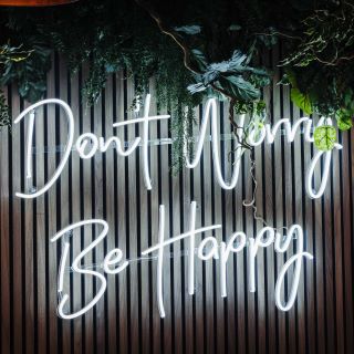 Don't Worry Be Happy white Naked Neon™ by Custom Neon® sign on dark wood panelled wall