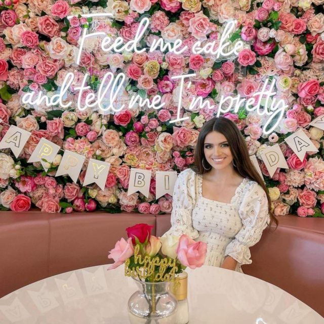 Feed Me Cake and Tell Me I'm Pretty Custom Neon® sign on a flower wall above a booth @plateddreamscafe