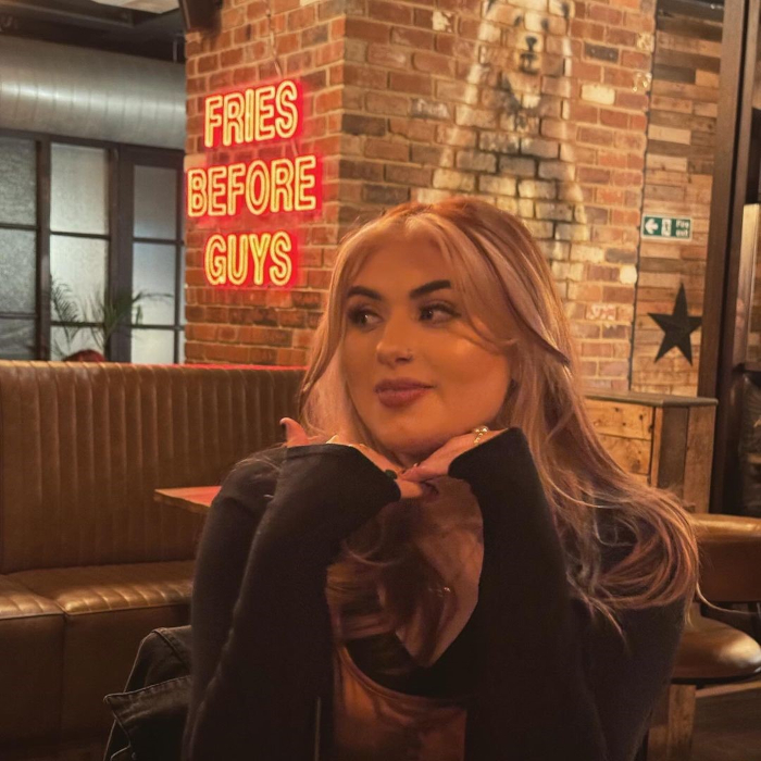 Selfie of a lady in @brewskirestaurants with a grisly bear mural and Fries Before Guys Custom Neon® sign on the brick walls