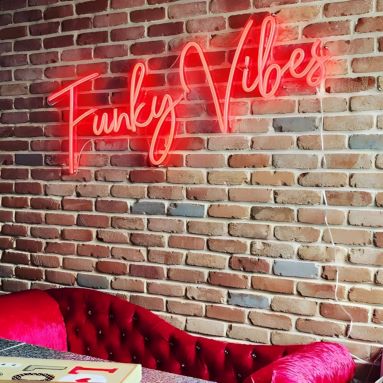 Funky Vibes red CustomNeon® sign on brick wall above a red chaise lounge @absternash