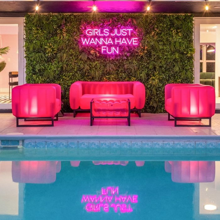 Girls Just Wanna Have Fun dark pink IP67 waterproof Custom Neon® sign on a grasswall beside the pool in an Airbnb designed by Somerled