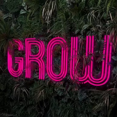 Custom Neon® pink triple lined GROW logo sign on a green plant wall @growplantbar