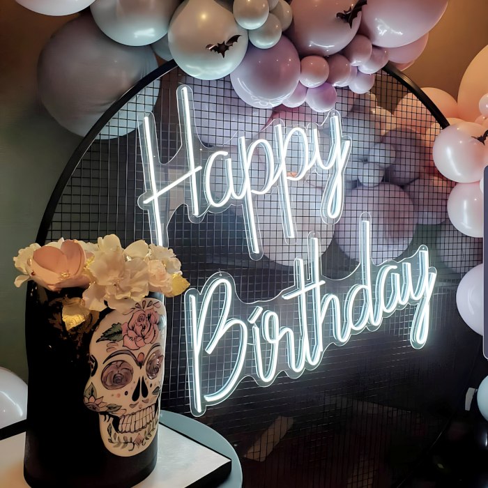 Custom Neon® white Happy Birthday sign on a black wire mesh frame topped with a purple and grey balloon garland and Dia de los Muertos party props - event decor by @decorandfiesta
