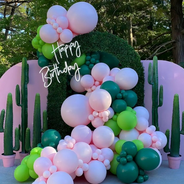 Custom Neon® Happy Birthday sign on a faux grass arch with balloons cascading through surrounded by cacti props - event decor by @decorandfiesta
