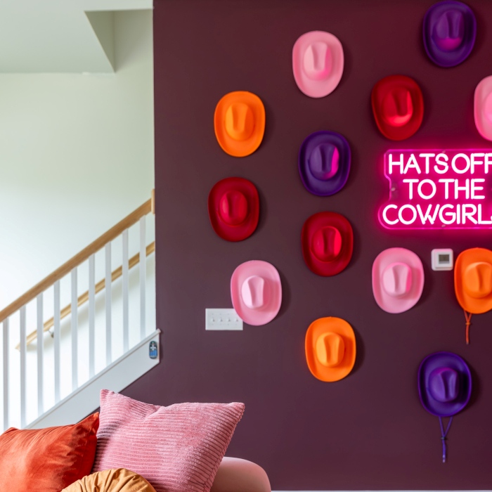 Hats Off to the Cowgirl hot pink LED Custom Neon® sign surrounded by cowgirl hats of various colors on a dark plum wall in a living room designed by Somerled