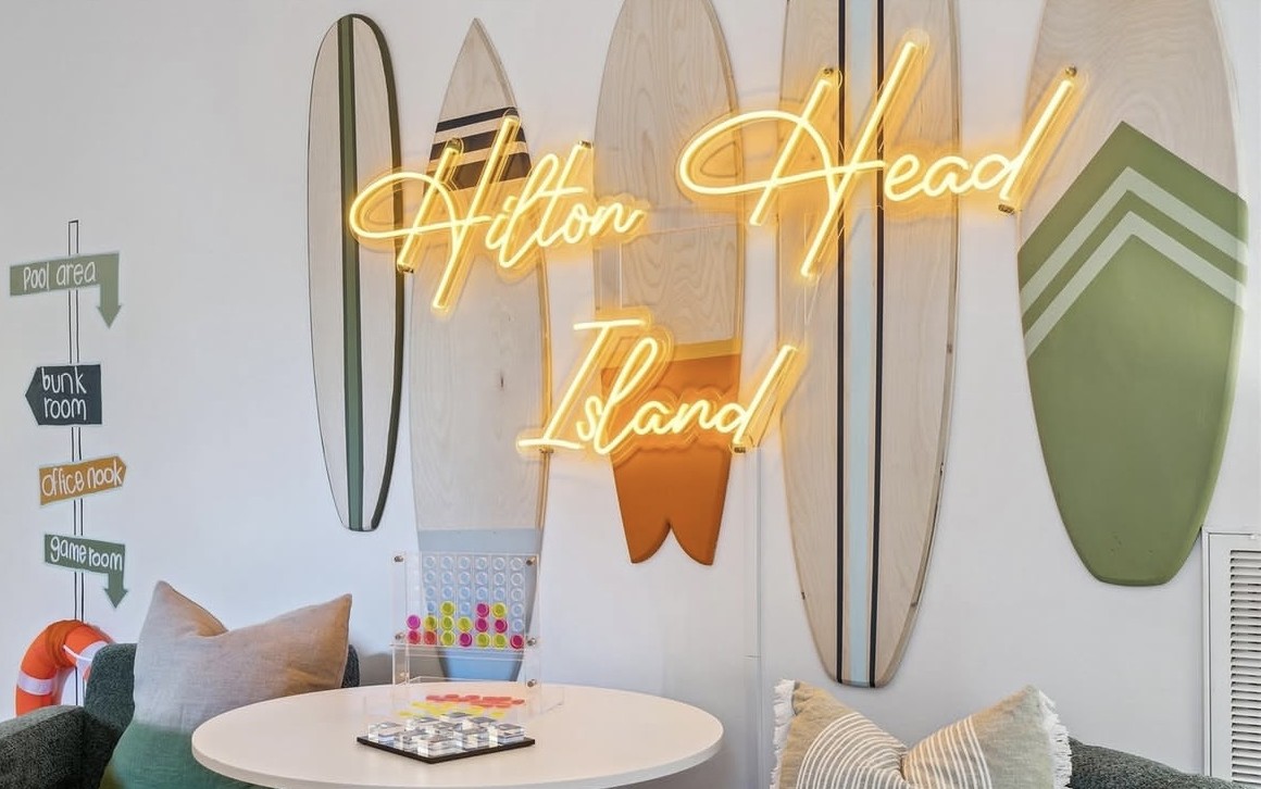 Hilton Head Island orange Custom Neon® sign hung against surfboards on a white wall in a vacation home designed by Somerled