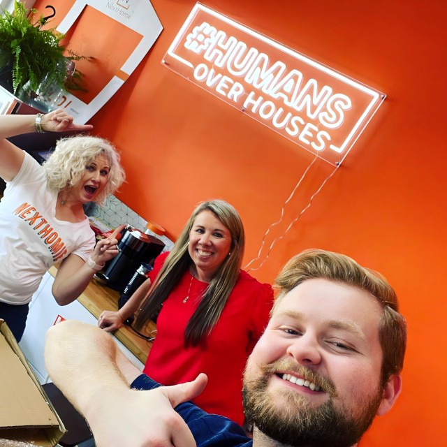 Custom Neon® white hashtag sign on an orange wall in the background of a group selfie @nexthomeourtown