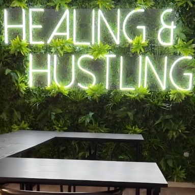 Custom Neon® Hustling & Healing motivational quote sign on green wall