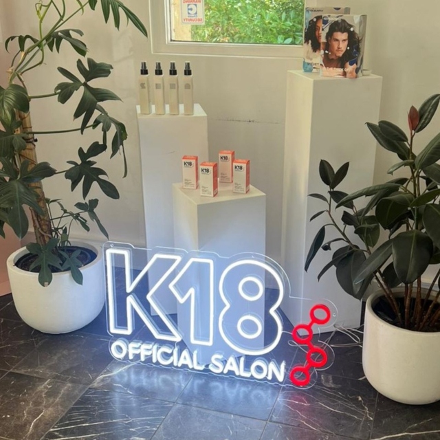 White and red logo sign on a grass wall in a hair salon by Custom Neon® @k18hair_australia
