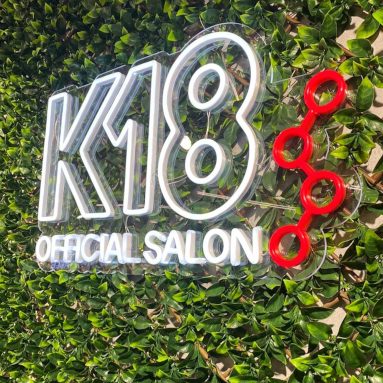 White and red logo sign on a grass wall in a hair salon by Custom Neon® @k18hair_australia