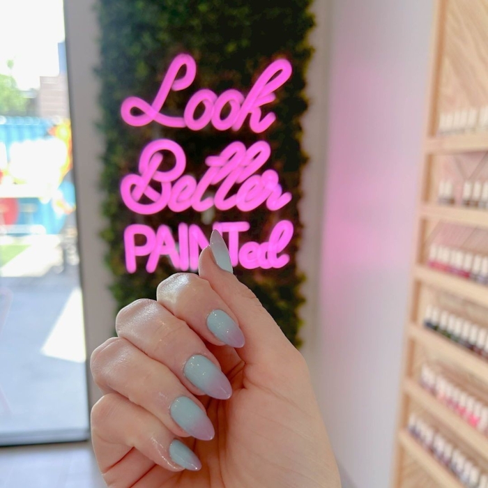 Look Better Painted Custom Neon® pink tagline sign on a grass wall at Painted Nail Bar