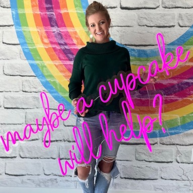 Maybe a cupcae will help pink LED Custom Neon® sign held by a lady in front of a pale grey brick wall with a rainbow mural