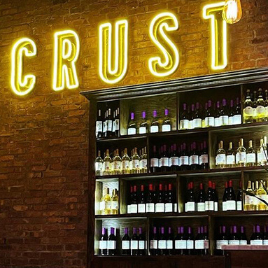 Custom Neon® yellow LED neon CRUST logo sign on brick wall in a Crust pizza restaurant