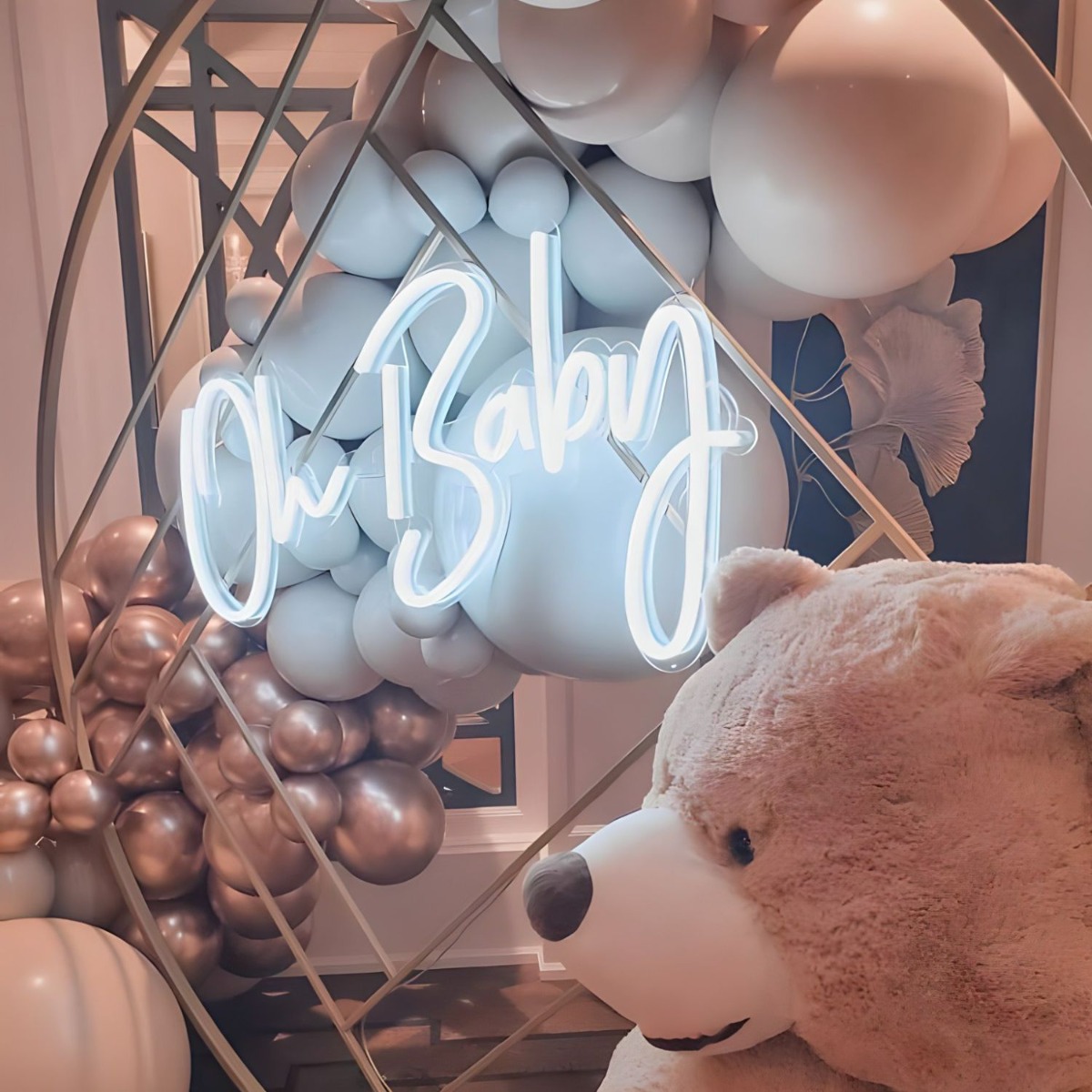 Custom Neon® white Oh Baby sign on a rose gold metal frame surrounded by a giant teddy bear, a balloon garland, teddy bear cakes and other neutral tone party props - event decor by @decorandfiesta