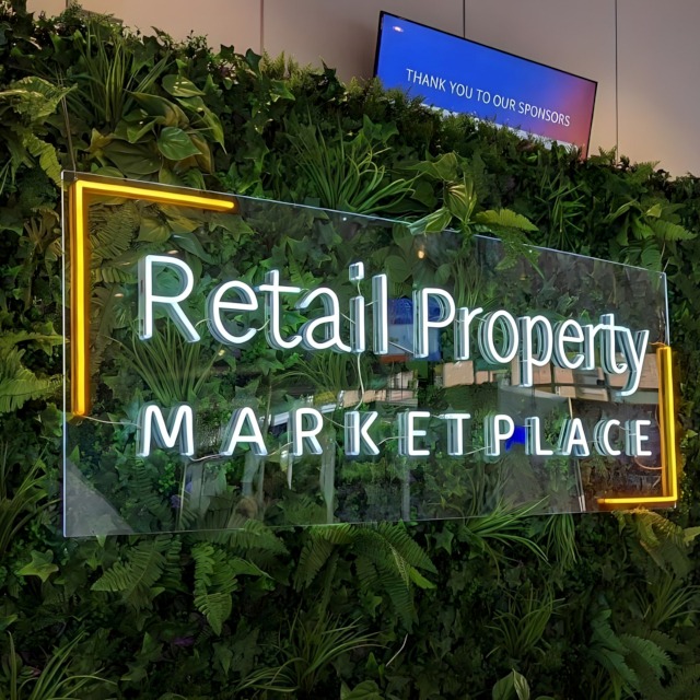 Custom Neon® @retailpropertymarketplace event sign hung from a grasswall