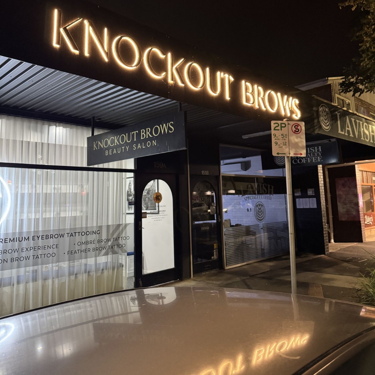 Gold mirrored stainless steel backlit storefront sign above the entrance to the Knockout Brows salon