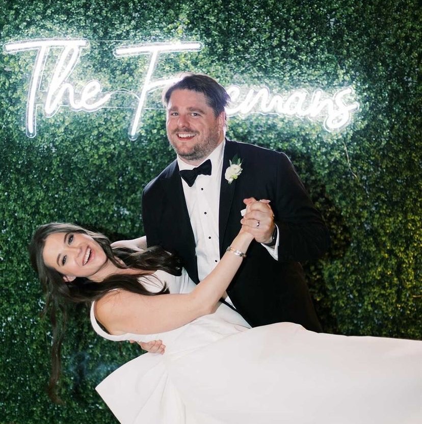 White Custom Neon® wedding last name sign on green wall behind the bride & groom