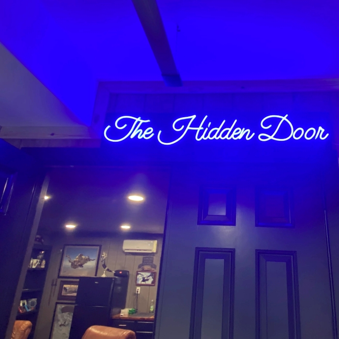The Hidden Door dark blue Custom Neon® man cave sign mounted above a black door