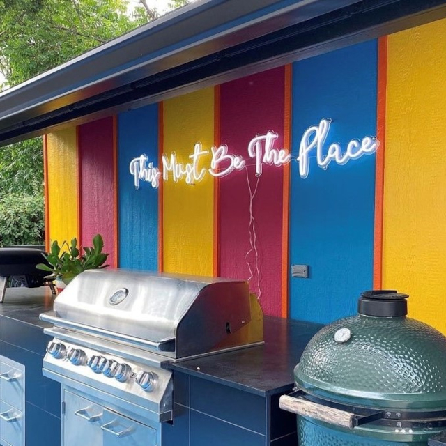 Custom Neon® white This Must Be the Place sign on a bright wall in an outdoor kitchen @shaunaglenn