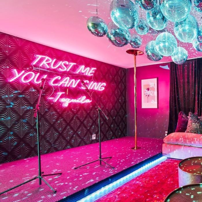 Trust Me You Can Sing - Tequila large pink LED Custom Neon® stage backdrop with a dancing pole and microphones in the foreground of a karaoke room designed by Somerled