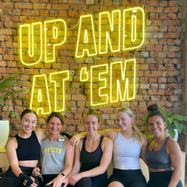 Custom Neon® yellow Up and At Em sign on a brick wall in the selfie station @upstate_studio