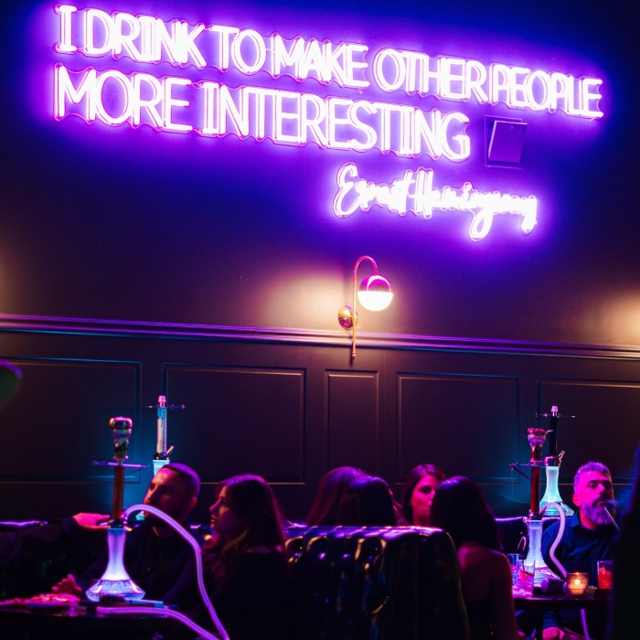 Purple Custom Neon® Hemmingway quote sign on a dark wooden wall above patrons @whiskytangobar